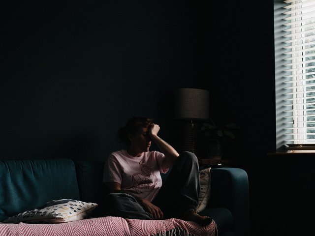 Lonely person sits on sofa with head in hands