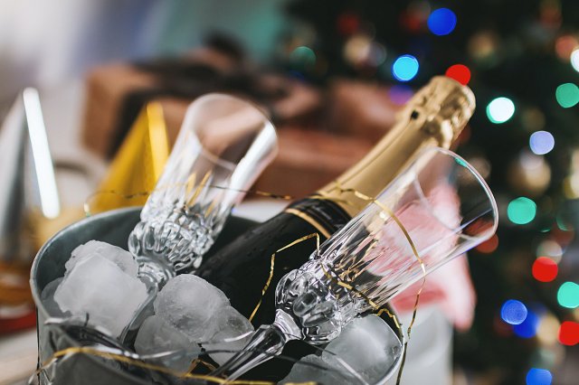 Champagne in an ice bucket with crystal glasses, lit up Christmas tree in the background